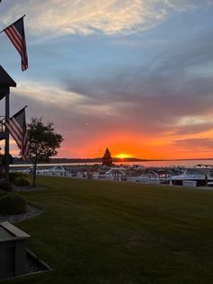 the sun is setting over a marina with boats in the water and an american flag flying