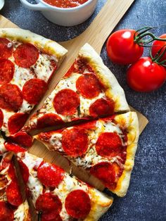 a pepperoni pizza cut into four slices on a cutting board next to tomatoes and ketchup