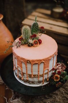 a cake with pink icing and cactus decorations on top is sitting on a black plate