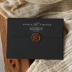 a black envelope with a wax stamp on it sitting on top of a wooden table