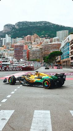 a green and yellow race car is on the track in front of some tall buildings