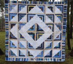 a blue and white quilt hanging from a clothes line in the grass with trees behind it