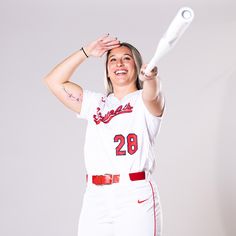 a woman in a baseball uniform is holding a bat and posing for the camera with her hands behind her head