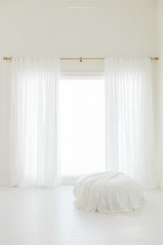 a white bed sitting next to a window in a room with curtains on the windowsill