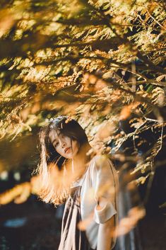 a woman standing under a tree with her hair blowing in the wind and looking up