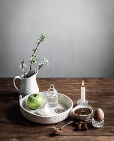 an assortment of food on a wooden table next to a white vase with flowers in it