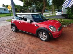 a small red car parked in front of a palm tree on the side of a road