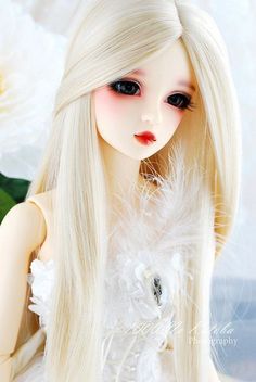 a white doll with long blonde hair and flowers in her hand, sitting on a table