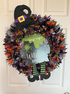 a halloween wreath on the front door decorated with witch's legs and witches hat