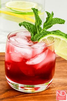 a red drink with lime and mint garnish sitting on a wooden cutting board