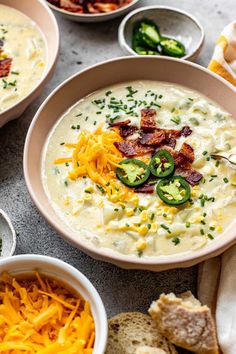 two bowls of soup with cheese, bacon and green peppers next to other dishes on the table