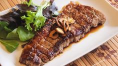 a white plate topped with meat and salad on top of a wooden table next to a fork