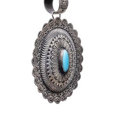 Length: 4" Width: 2 3/4" This pendant handcrafted by Shawn Cayatineto features a traditional concho design with incredibly detailed silver-work. An oval shaped Sleeping Beauty Turquoise stone sits at the center, encased in a sawtooth bezel. The surrounding sterling silver is decorated with hand-stamped designs that effortlessly draw the eye and are completed by the concho's scalloped edges--also replete with stunning details. Finally, the pendant is finished with a hand stamped bail to complete this intricate and unique piece. Traditional Hand Tooled Turquoise Jewelry, Silver Concho Pendant Jewelry, Traditional Silver Turquoise Necklace With Large Pendant, Traditional Turquoise Necklace With Concho, Traditional Silver Turquoise Necklace With Concho, Southwestern Turquoise Necklace With Oval Pendant, Traditional Turquoise Concho Necklace, Traditional Turquoise Jewelry With Concho, Traditional Silver Turquoise Concho Necklace