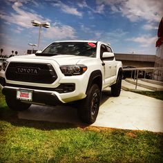 a white toyota pickup truck parked in front of a building with blue sky and clouds