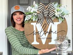 a woman holding up a welcome to our home sign with flowers in the front door