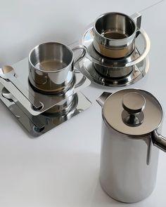 three stainless steel pots and pans sitting on top of a white table with silver handles