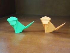 two origami dinosaurs sitting next to each other on a wooden floor in front of a wall