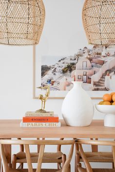 a white vase sitting on top of a wooden table next to oranges and books