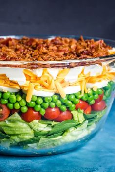 a layered salad in a glass bowl on a blue surface