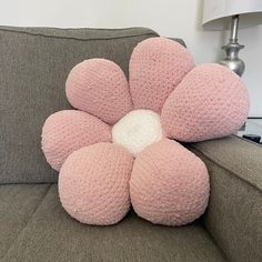 a crocheted pink flower pillow sitting on top of a couch next to a lamp