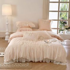 a white bed with pink comforter and pillows on it in a room next to a window