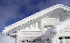 a house covered in snow and icicles under a blue sky with clouds behind it