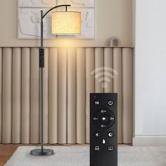 a black remote control sitting on top of a white rug in front of a lamp