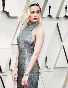 a woman in a silver dress standing on a red carpet at an oscars event