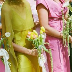 two women in pink and yellow dresses are holding bouquets with flowers on each side