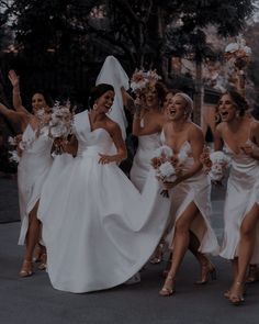 a group of bridesmaids in white dresses walking down the street with their arms in the air