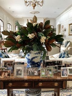 a vase with flowers on a table in a living room filled with furniture and pictures