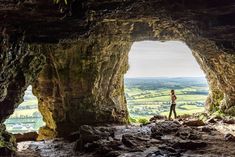 a person standing in the middle of a cave looking out at the valley and countryside