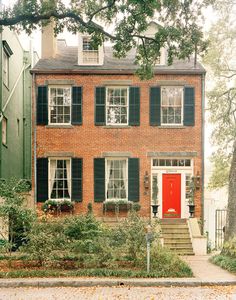 a brick house with green shutters and red door