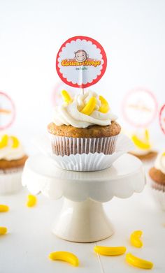 a cupcake with white frosting and yellow sprinkles on a cake stand