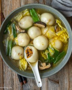 a bowl filled with dumplings and vegetables on top of a wooden table next to chopsticks