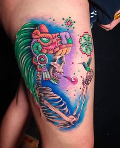 a woman's thigh with a colorful tattoo design on it and a skeleton holding a pipe