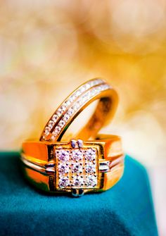 two gold wedding rings sitting on top of a blue velvet covered box with diamond accents