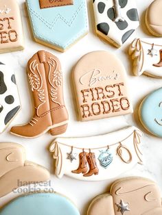 cookies decorated with cowboy boots and other items on a white tablecloth that says first rodeo