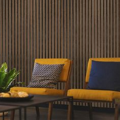 two yellow chairs sitting next to each other in front of a wooden wall with vertical blinds