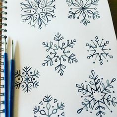 a notebook with snowflakes drawn on it next to two markers and a pencil