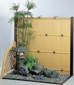 a bamboo fence with some plants and rocks in it next to a small lantern on the ground