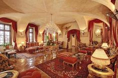 an ornate living room with red and gold curtains, chandelier, couches, tables and chairs