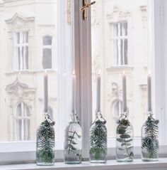 three glass bottles with plants in them sitting on a window sill next to candles