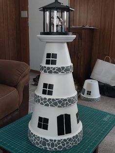 a white lighthouse with black windows and a light on it's top sitting on a green mat