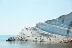 many people are standing on the edge of an ice - covered cliff by the water