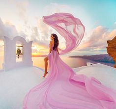 a woman in a pink dress standing on top of a white building next to the ocean