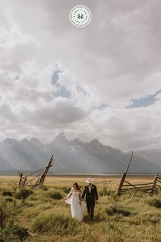 a bride and groom are walking through the grass with mountains in the background at their wedding