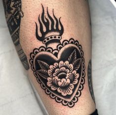 a black and white photo of a heart tattoo on someone's leg with flames coming out of it