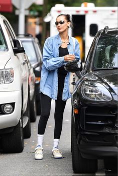 a woman in black leggings and sneakers is walking down the street with her hand on her hip