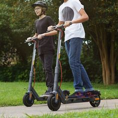 two young men are riding electric scooters in the park